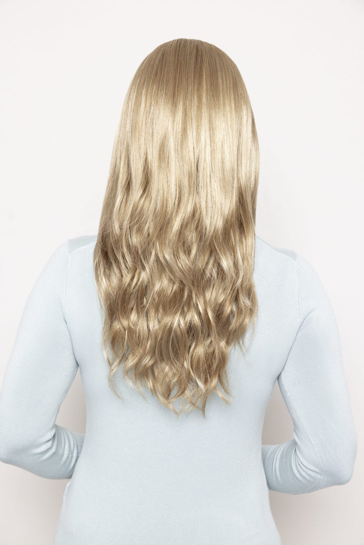A long, wavy blonde wig with a soft golden-blonde color, shown from the back on a model wearing a light blue long-sleeve top against a plain white background.