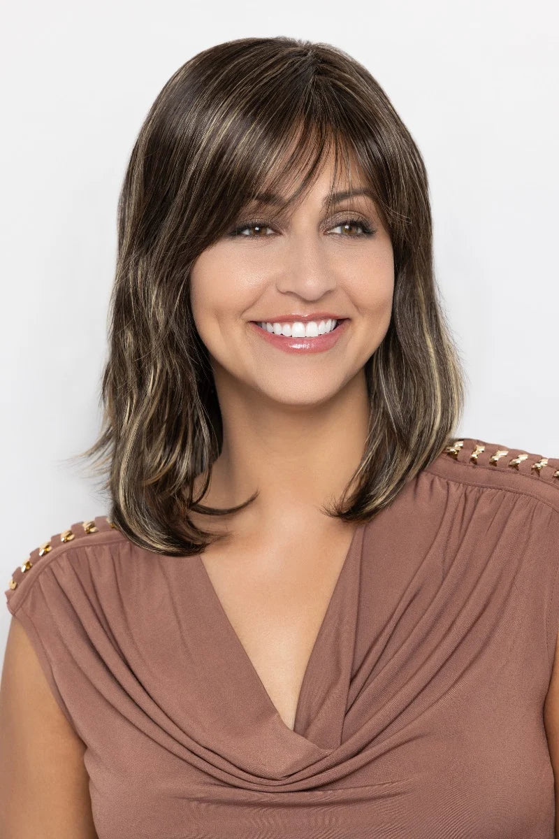 A smiling woman with shoulder-length brown hair with lighter brown highlights, wearing a brown draped top against a light gray background.