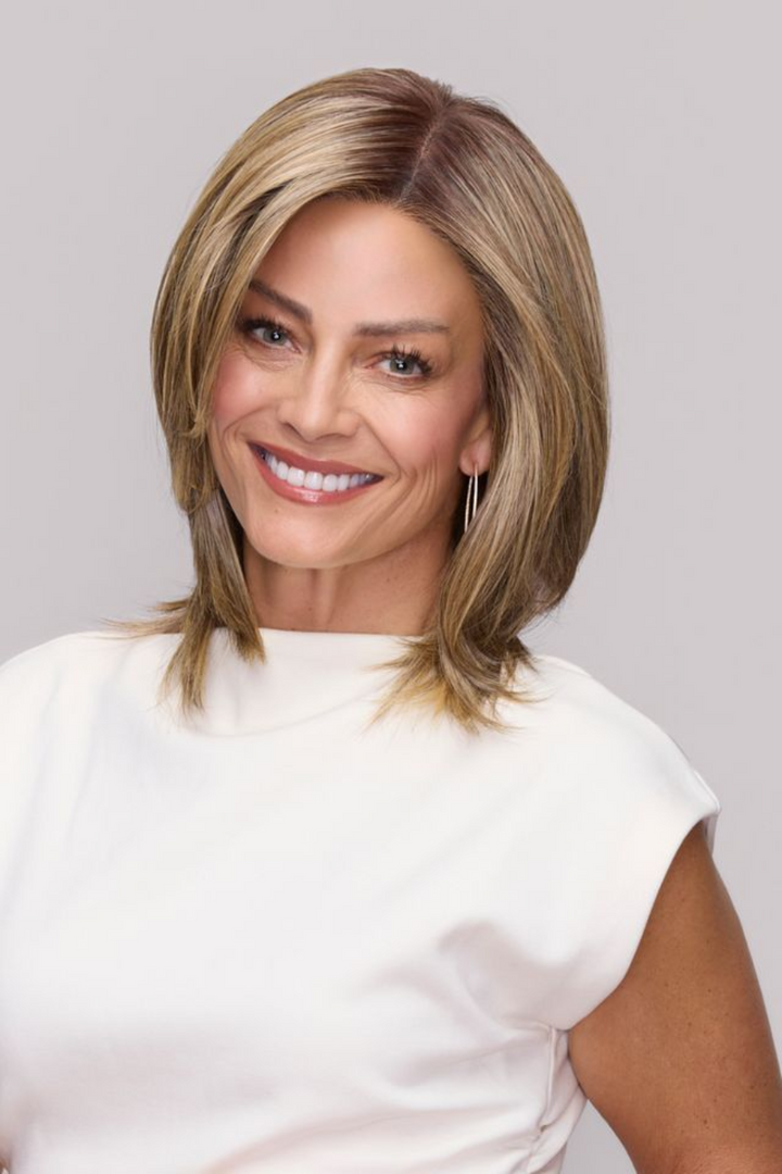 A smiling woman with shoulder-length blonde hair wearing a white top, photographed against a light gray studio background.