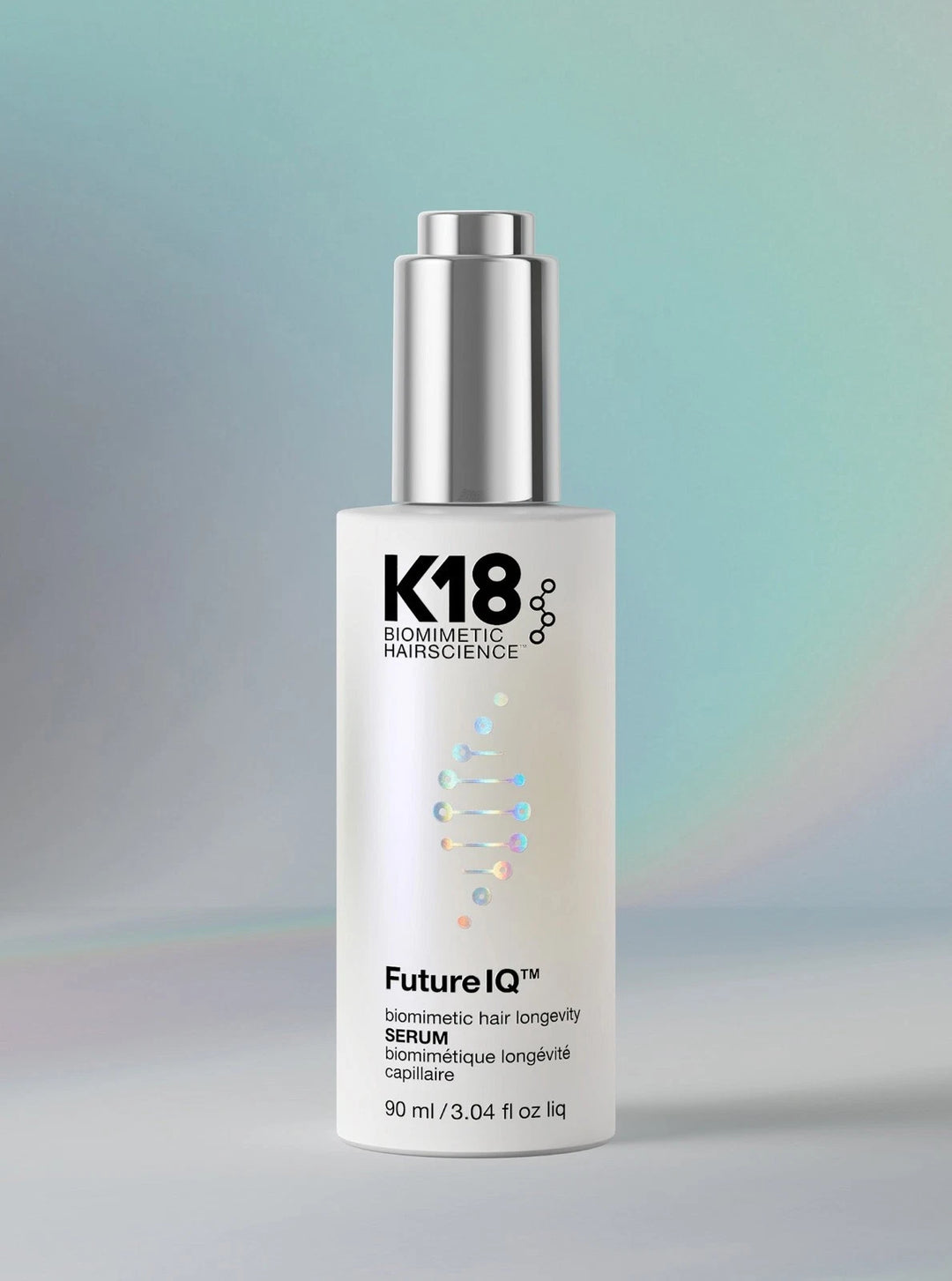 K18 Biologics Future IQ Serum bottle with a silver pump and white label, set against a soft gradient background of teal and gray.