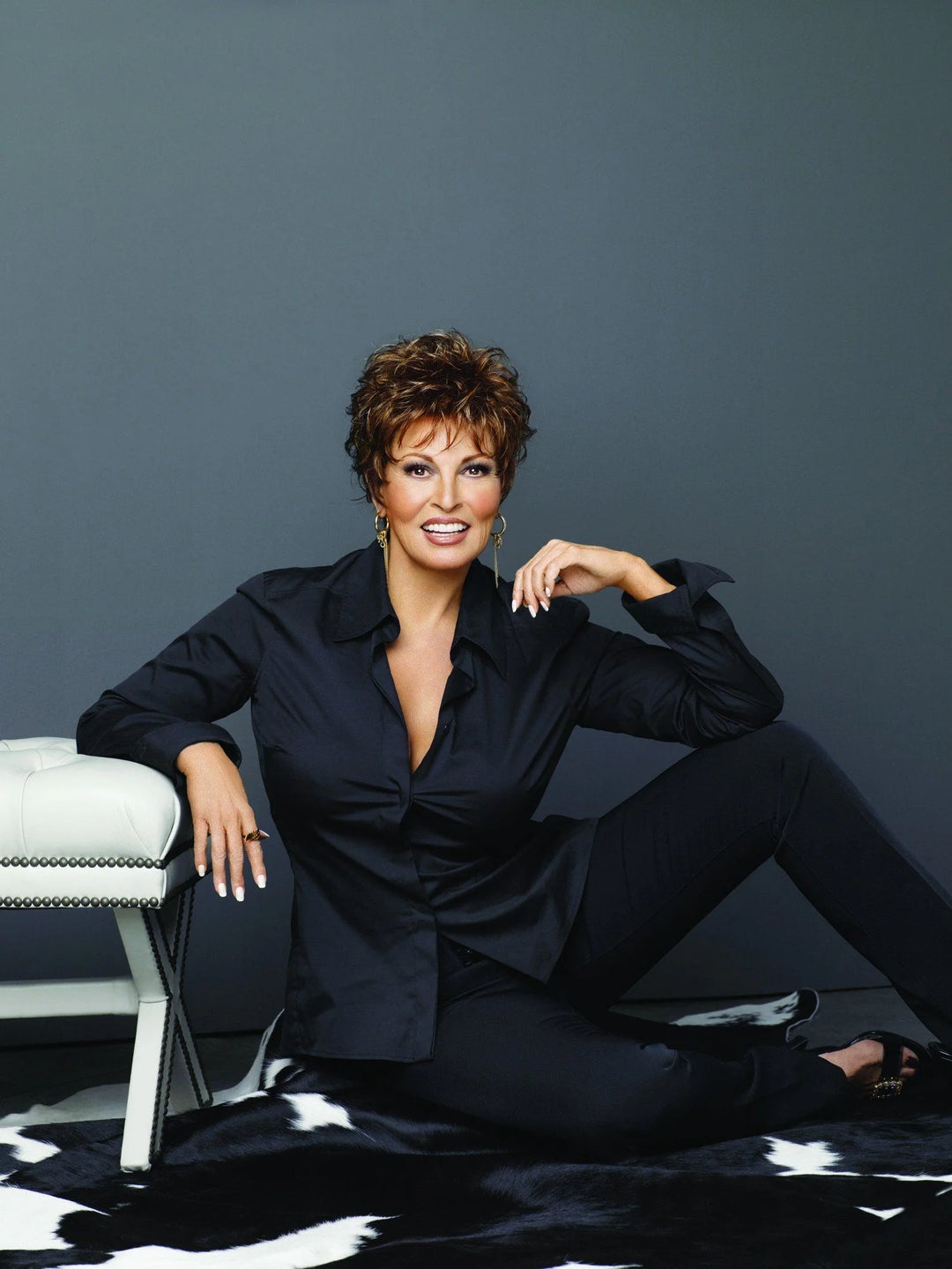 Woman in a black outfit sitting on a white chair against a gray background