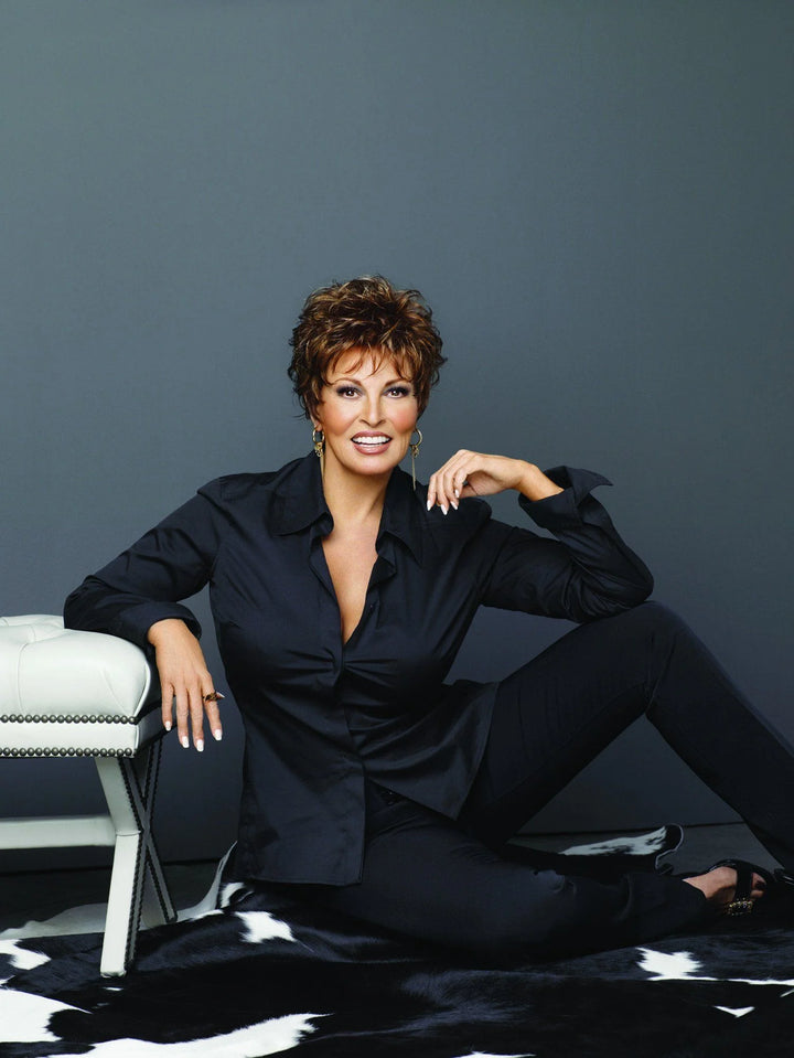 Woman in a black outfit sitting on a white chair against a gray background